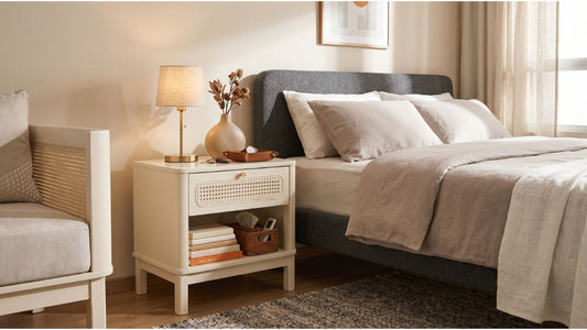 Cream bedside table with open storage shelf, woven basket, lamp, and upholstered bed in a modern Singapore bedroom