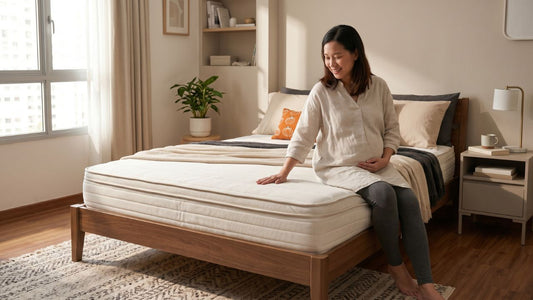 Pregnant woman sitting on a supportive mattress in a warm Singapore bedroom with wooden bed frame and bedside table